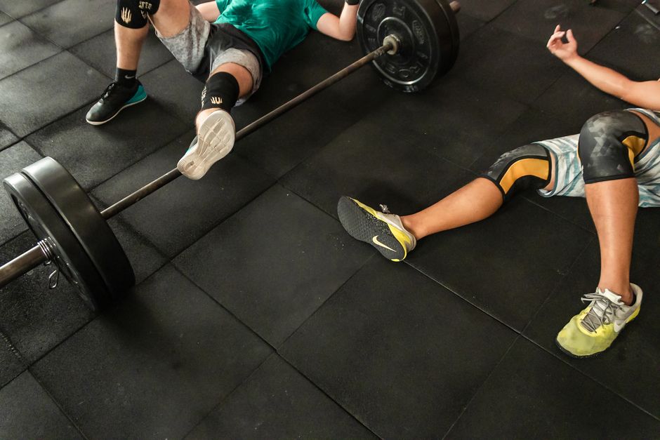 Athletes resting on a gym floor beside heavy barbells after an intense weightlifting session