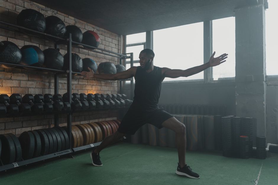 A muscular black man stretching in a modern gym